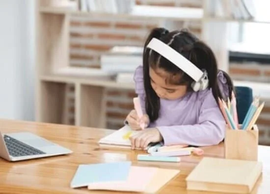 ヘッドフォンをつけてノートに書き込みながら学ぶ小学生