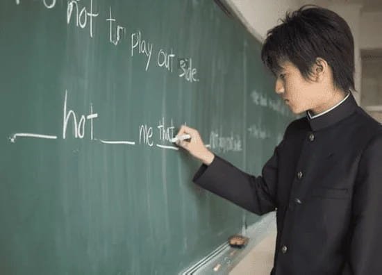 Student writes an English lesson on the chalkboard in a classroom.