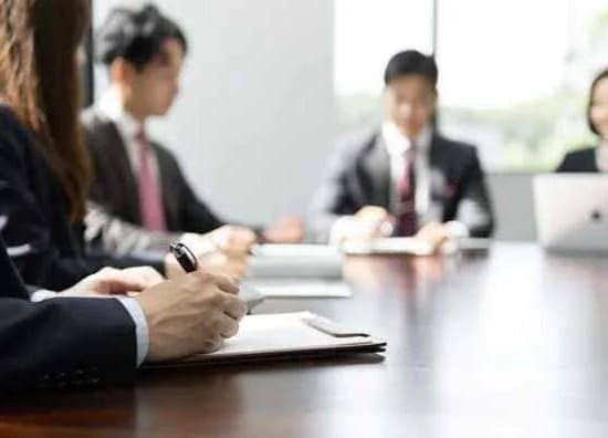 スーツ姿のビジネスチームが会議で英語の議論をしながらメモを取っている様子。